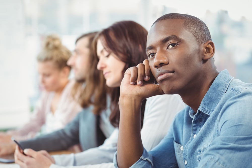 Thoughtful man sitting at desk with coworkers in office Thoughtful man sitting at desk with coworkers in office